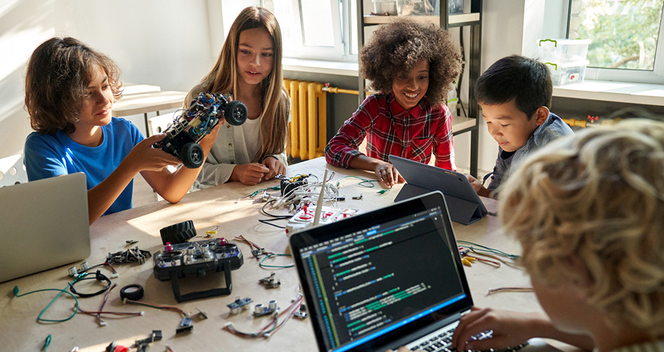 Diverse school children students build robotic cars using computers and coding.