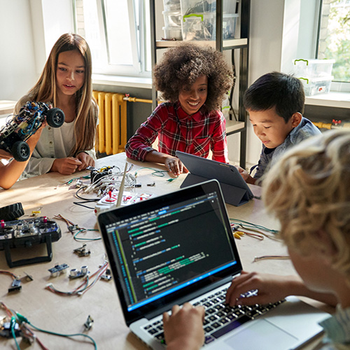 Diverse school children students build robotic cars using computers and coding.